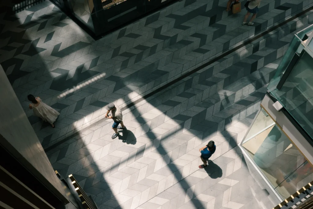 Arial image of a shopping mall with harsh light beams and shadows framing two shoppers.