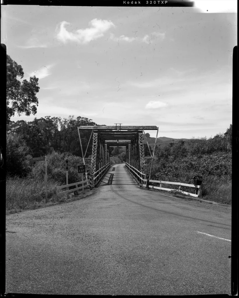 A large format black and white sheet film photograph of a three way intersection leading into a bridge.
