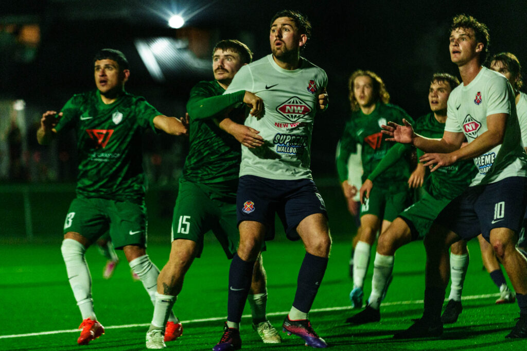 A group of football players fight for possession as they receive a corner kick.