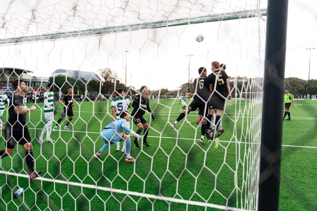 Auckland United FC players leap to defend an attacking header from Western Springs FC players.