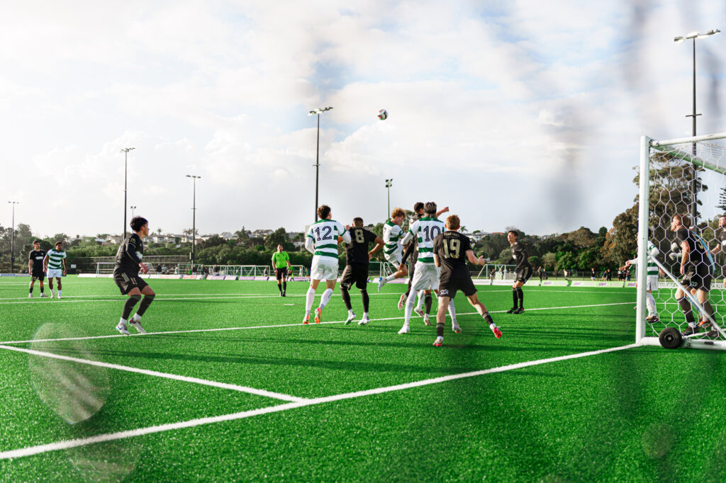 A wide photo of a football game shot through a fence.